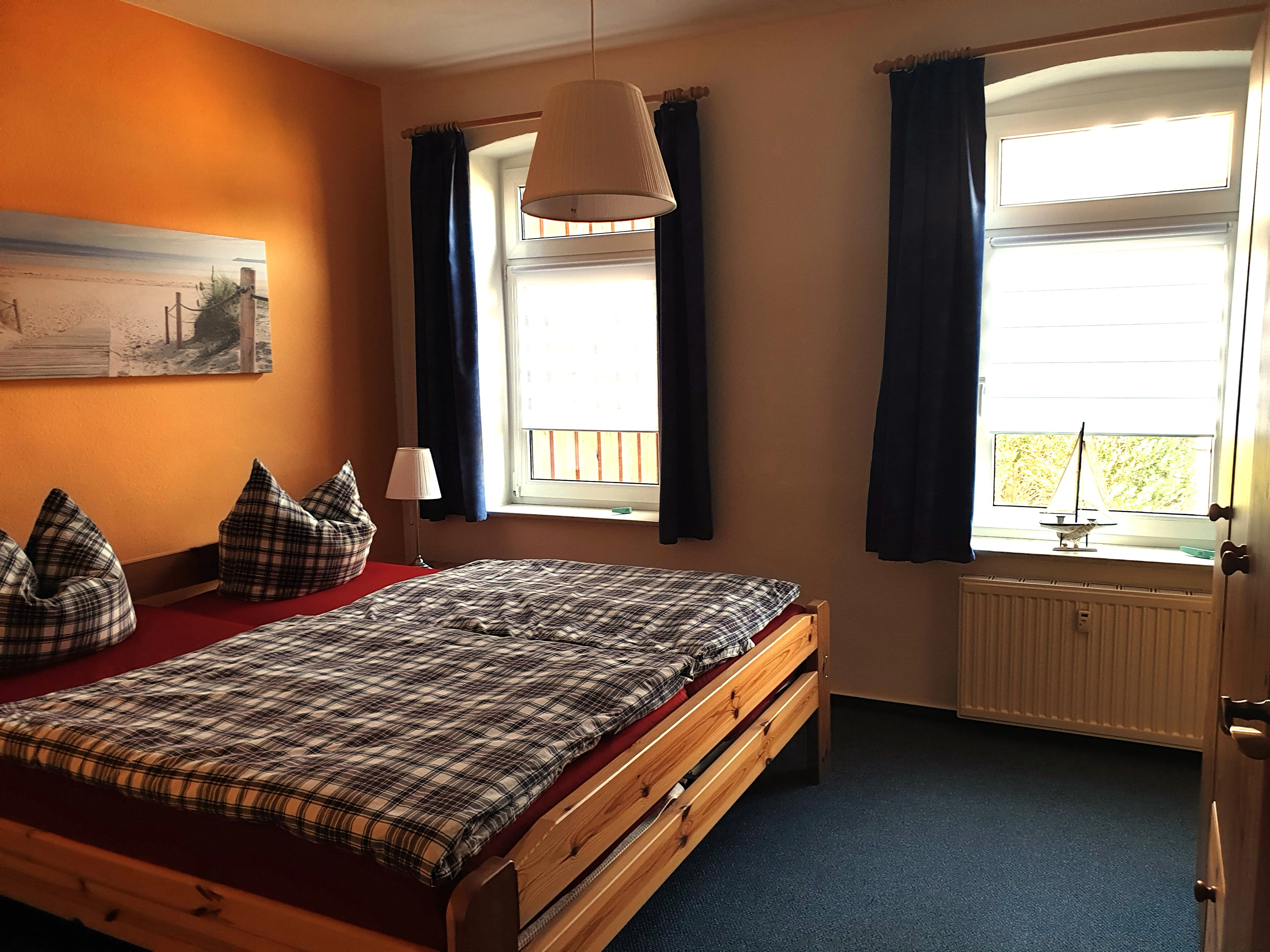Schlafzimmer der Erdgeschosswohnung mit hölzernem Doppelbett, Nachtschränken, Kleiderschrank und einem Ostsee-Strandbild über dem Bett