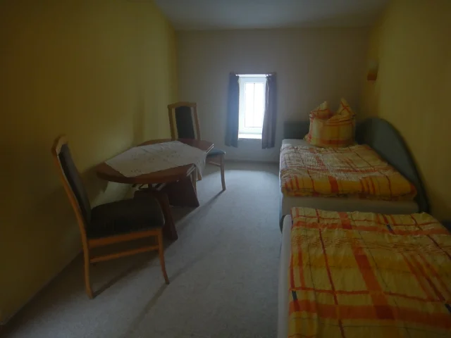 Zweitschlafzimmer der Obergeschosswohnung mit zwei Einzelliegen, Schrank, Tisch und Stühlen